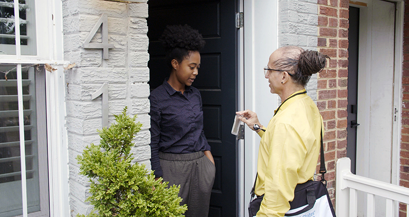 picture shows census worker at front door of home displaying his badge to homeowner
